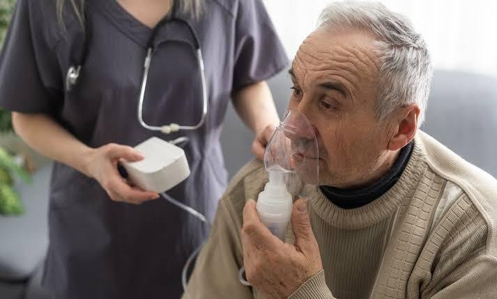 Older man using a nebulizer while a healthcare professional assists him, illustrating nebulizer therapy for COPD and respiratory conditions.
